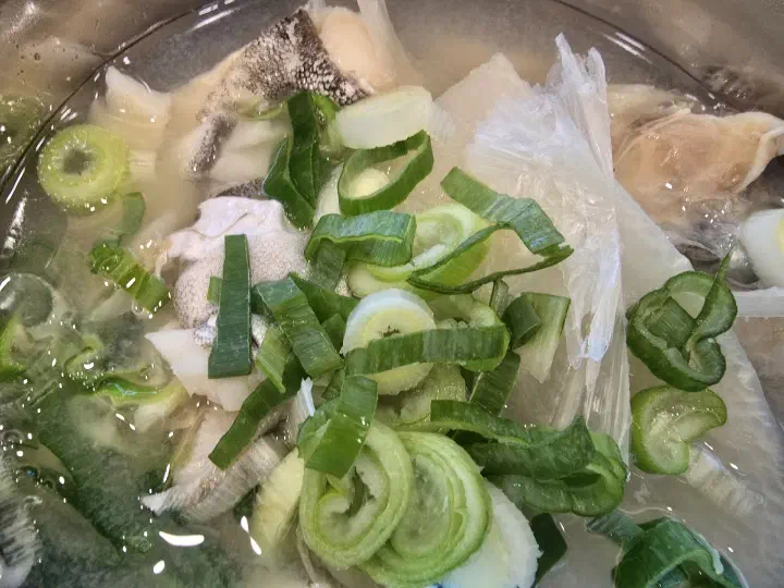 Top-down close-up of Haeundae Giwajip Daegutang cod soup with green onion and radish