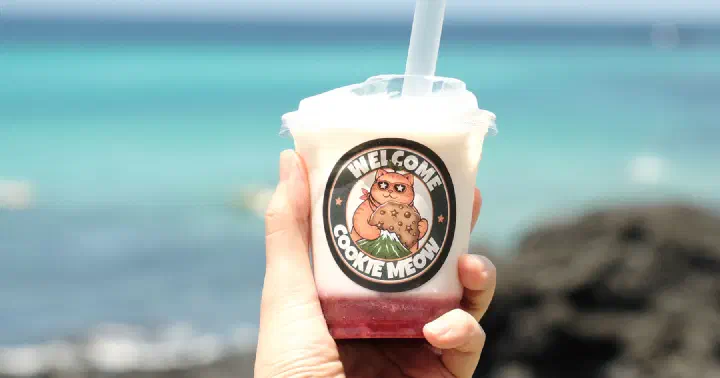 Jeju ttalgi jumulleok strawberry milk in a cat-logo cup held in front of the sea