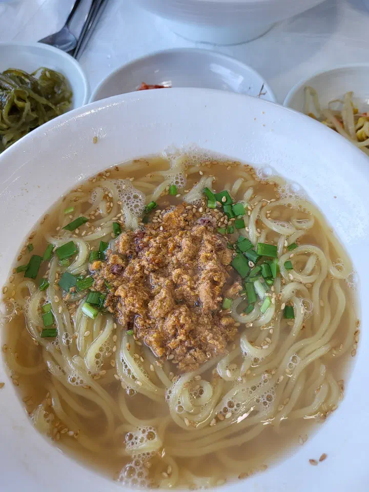 Gommak Sikdang seongge-guksu, sea urchin noodle soup in a clear broth topped with sea urchin and chopped scallions