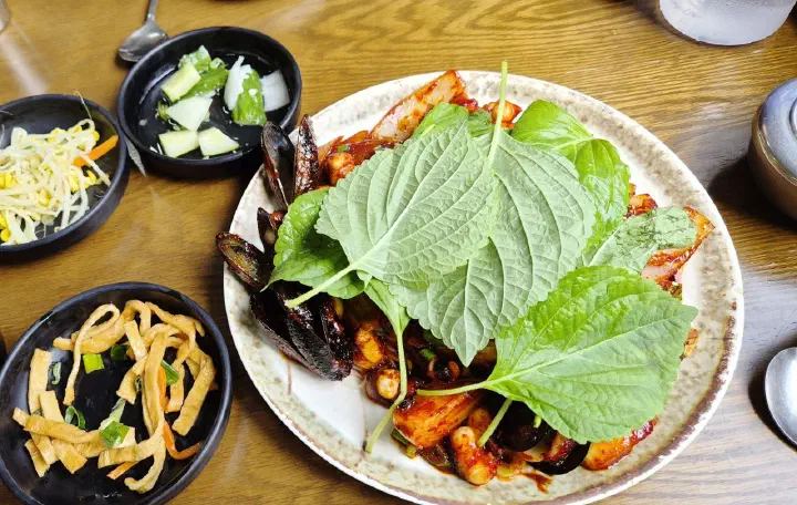 Perilla leaves lifted aside to reveal mussels and onions in the spicy octopus stir-fry