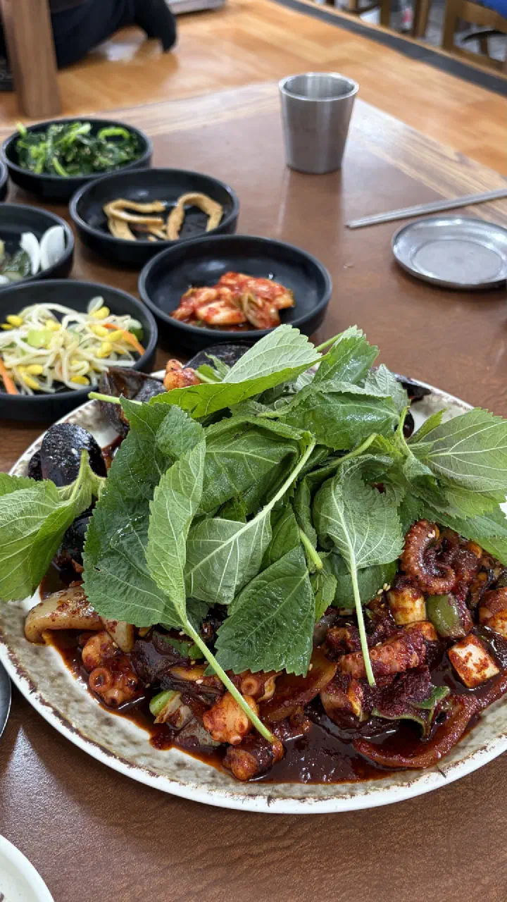 Stir-fried rock octopus platter buried under fresh perilla leaves, served with banchan at Sogeumbachi Sooninae