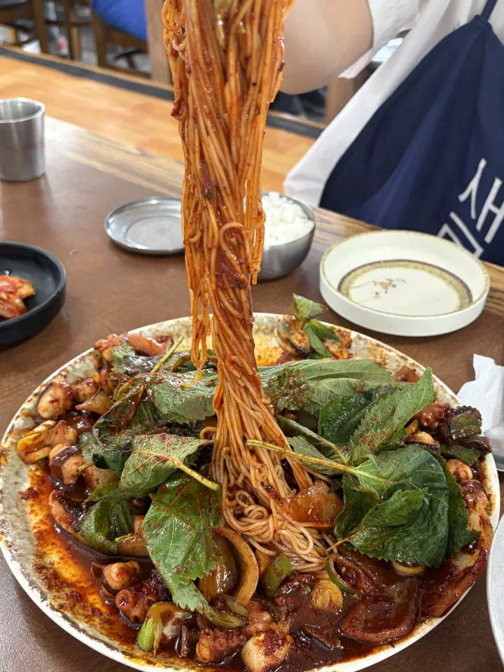 Chopsticks lifting somyeon noodles coated in the red octopus stir-fry sauce