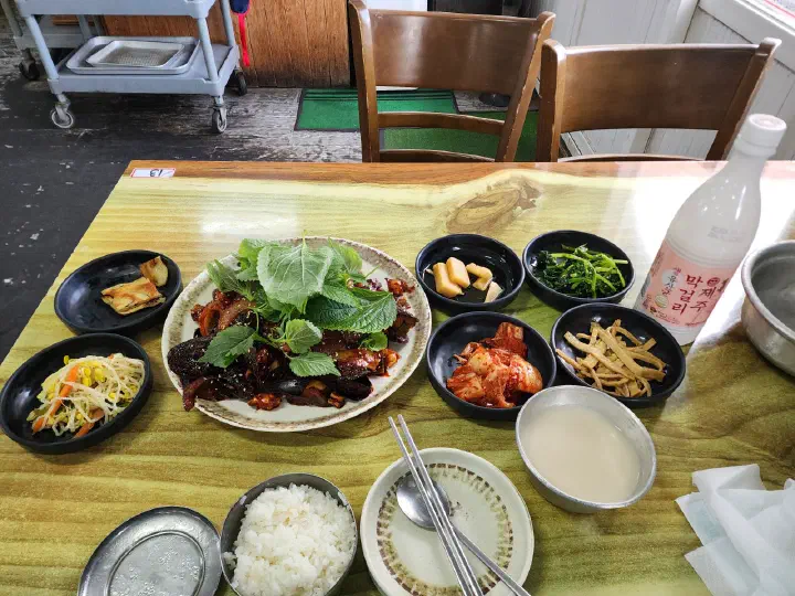 Full table setting at Sogeumbachi Sooninae with the octopus stir-fry, rice, banchan, and Jeju makgeolli