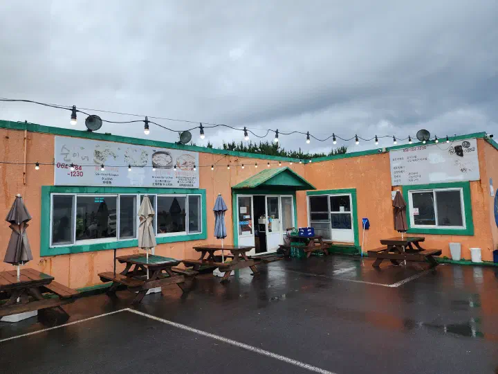 Orange exterior of Sogeumbachi Sooninae restaurant in Jongdal-ri, Gujwa, Jeju, with outdoor waiting tables