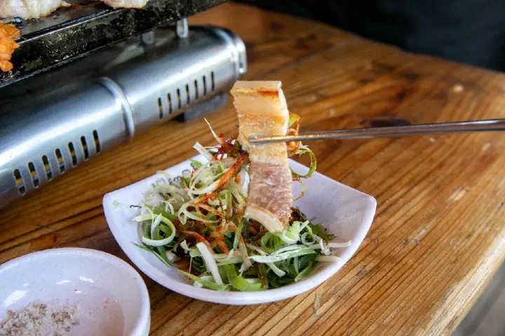 A piece of charcoal-grilled Jeju black pork placed on shredded green onion salad at Haeoreum
