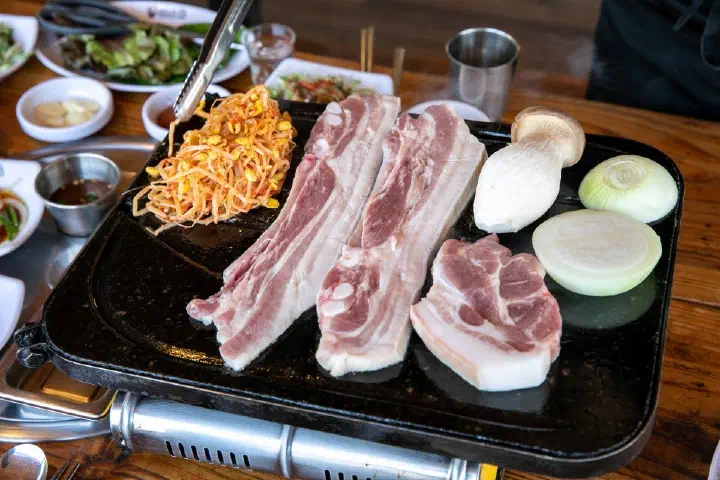 Jeju black pork belly grilling on the griddle with seasoned soybean sprouts