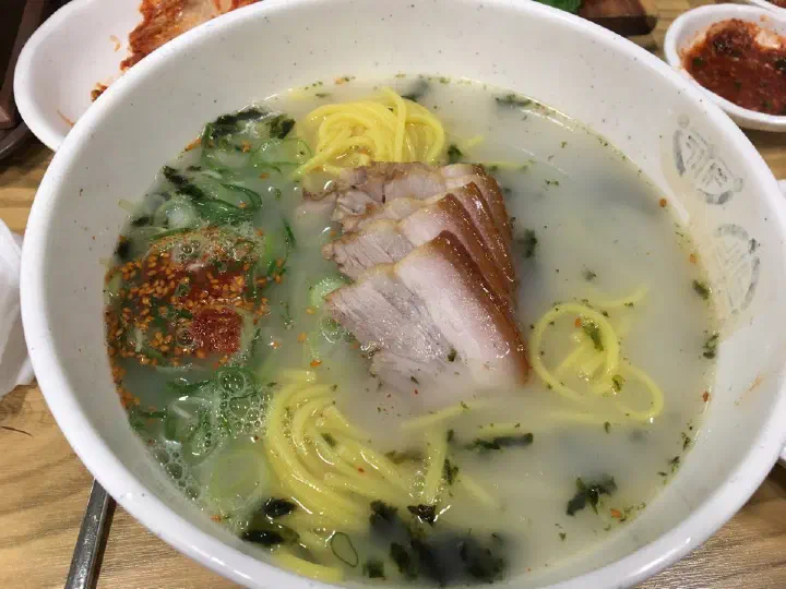 Close-up of Jamae Guksu gogi-guksu, rich pork-bone broth topped with sliced boiled pork