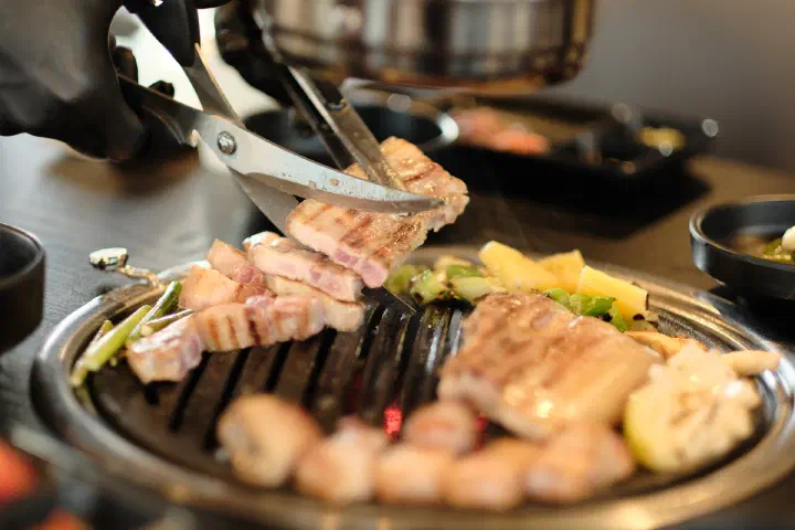Grilled Jeju black pork belly being cut into bite-sized pieces with kitchen scissors