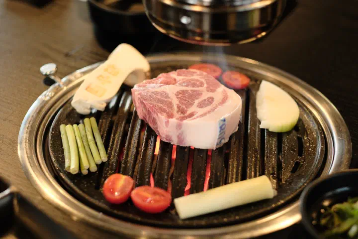 A thick slab of Jeju black pork neck set over glowing charcoal