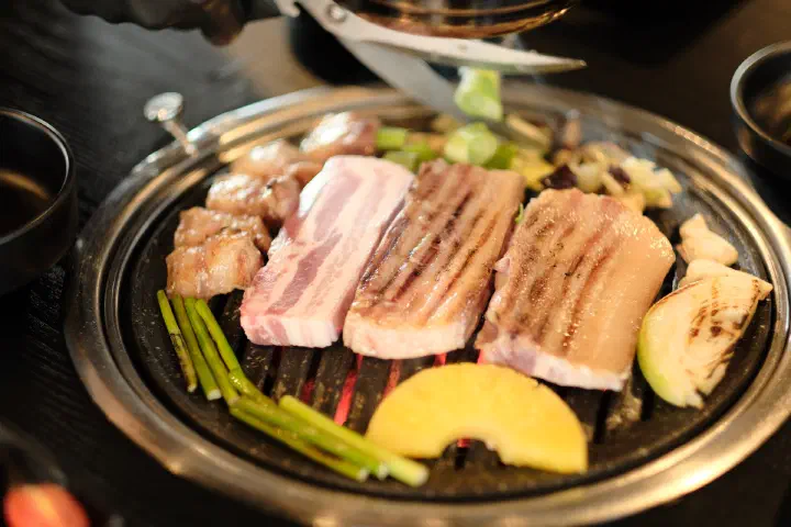 Thick-cut Jeju black pork belly grilling next to a slice of pineapple