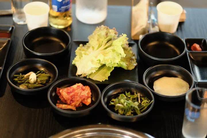 Banchan side dishes at Udam — lettuce, kimchi, and seasoned greens in black bowls