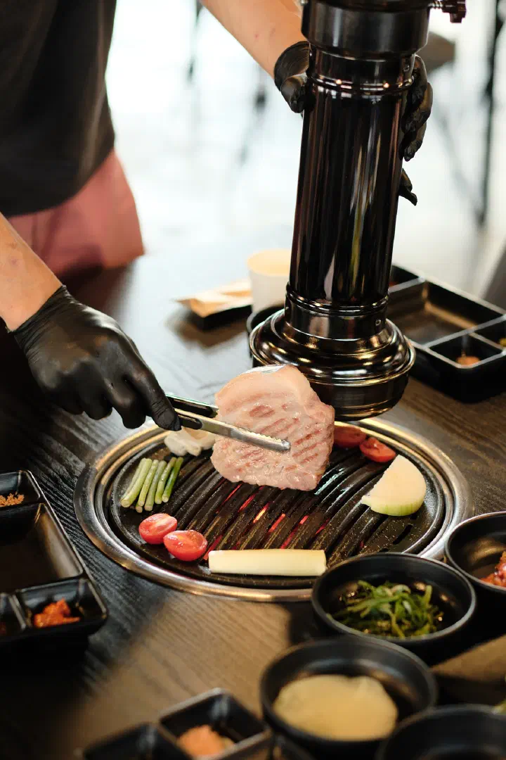 The owner turning a piece of Jeju black pork with tongs at the table