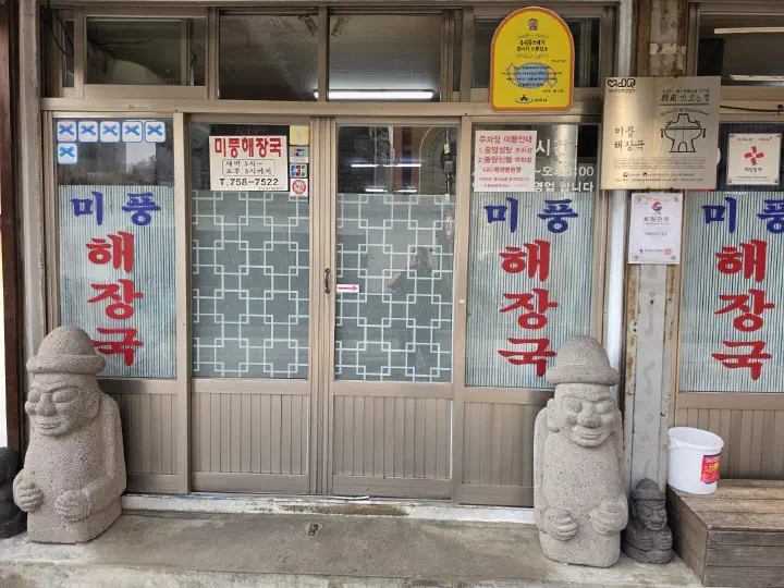 Entrance door of Mipung Haejangguk with posted opening hours and parking guide