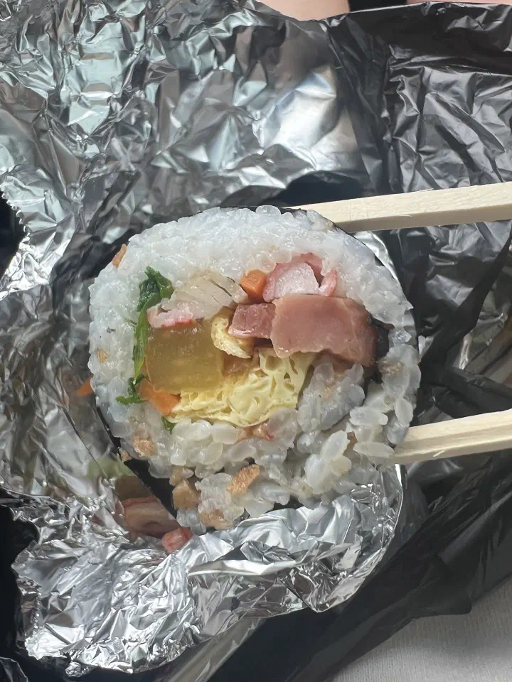 Cross-section of an Oneunjeong gimbap roll held with chopsticks, showing fried tofu and ham