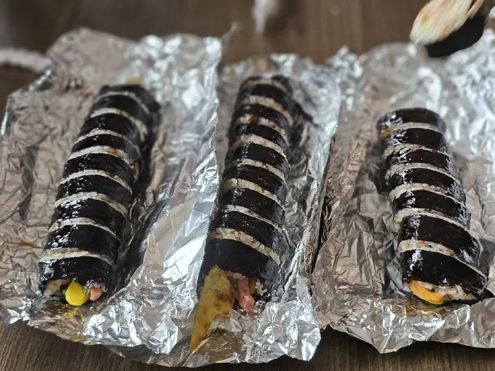 Three Oneunjeong gimbap rolls lined up on aluminum foil
