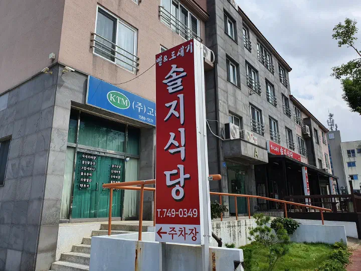 Tall red street sign for Solji Sikdang on Wollang-ro pointing to the free parking lot