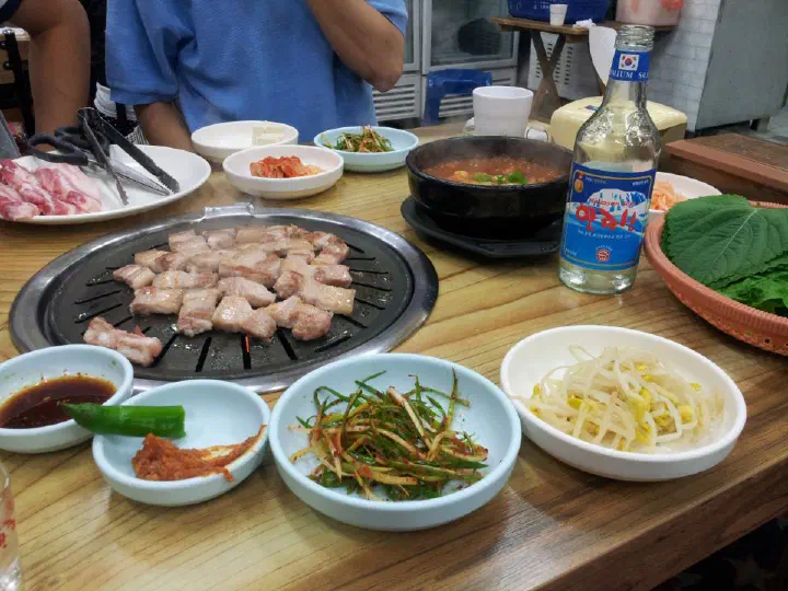 Ogyeop-sal pork belly grilling next to a pot of mel-jorim on a table at Solji Sikdang