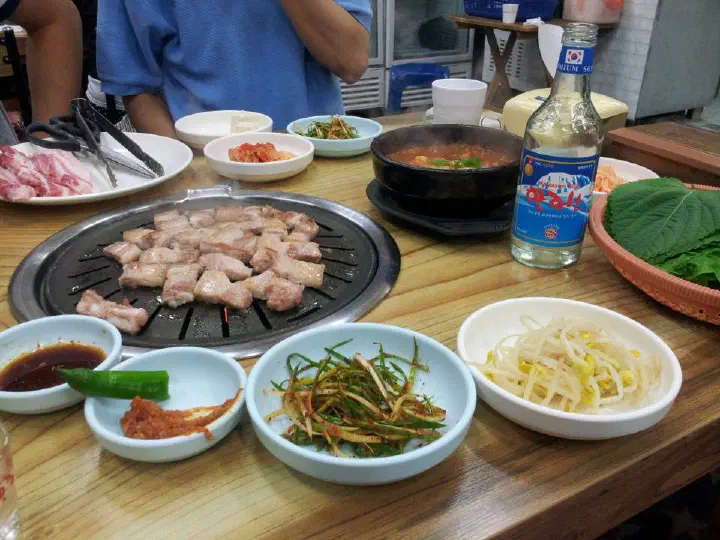 솔지식당 불판에 익어가는 오겹살과 멜조림 뚝배기가 놓인 테이블