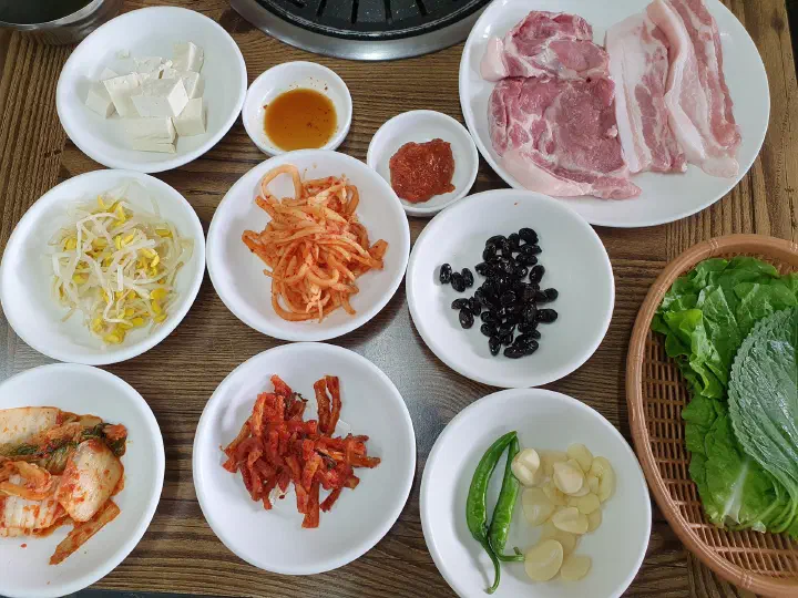 Solji Sikdang banchan spread of tofu, bean sprouts, kimchi, lettuce and raw pork