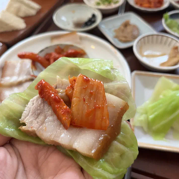 쌈채소에 수육과 김치를 올려 싼 애호락 보쌈 한 점