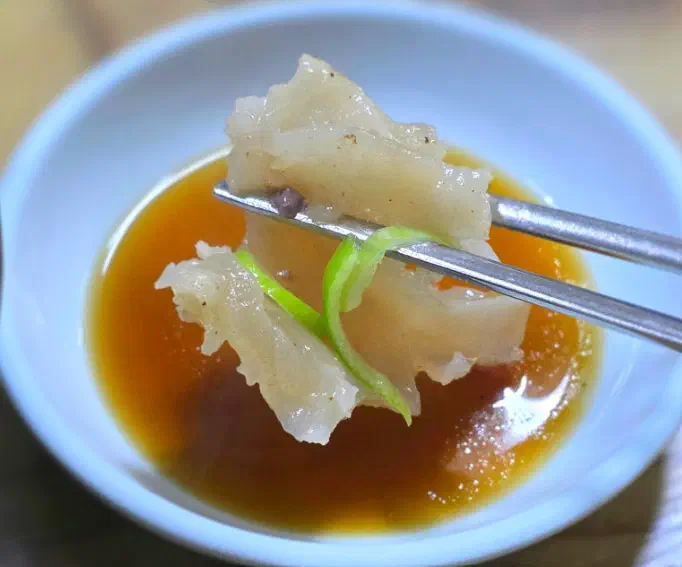 Close-up of a piece of Daesungjip ox-knee cartilage dipped in soy sauce