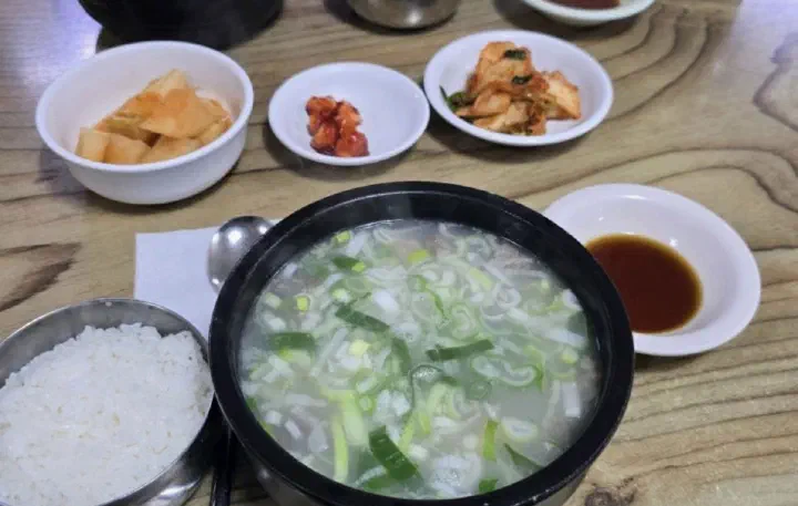 Daesungjip dogani-tang full table setting with rice and banchan of kkakdugi, seasoned garlic, and cabbage kimchi
