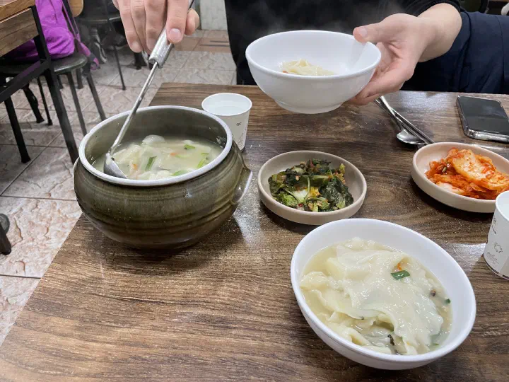 Ladling Samcheongdong Sujebi into individual bowls with napa and yeolmu radish kimchi on the side