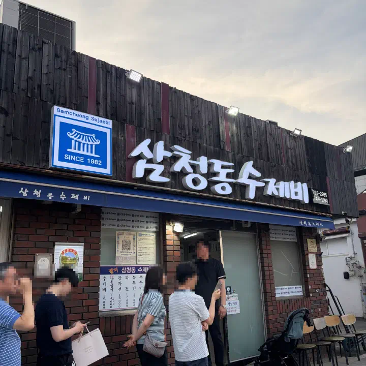 Blue storefront sign of Samcheongdong Sujebi reading Since 1982 with customers waiting in line outside