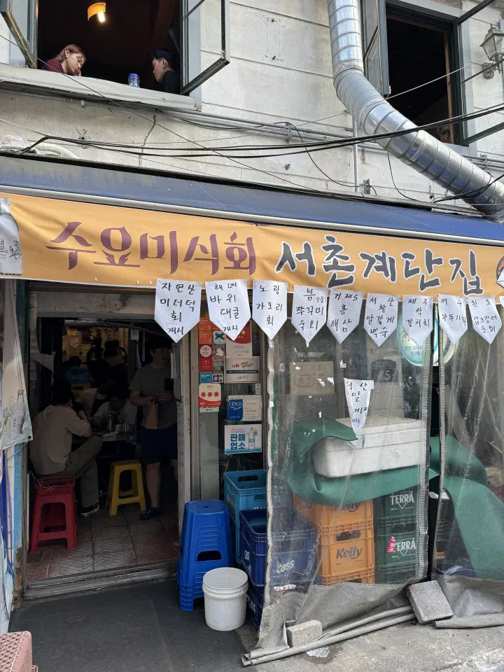 Crowded entrance of Seochon Gyedanjip with its Wednesday Food Talk banner and paper menu flags