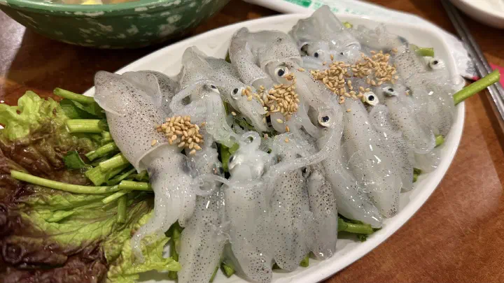 Kkolttugi-hoe, raw beka squid topped with sesame seeds on a bed of water dropwort