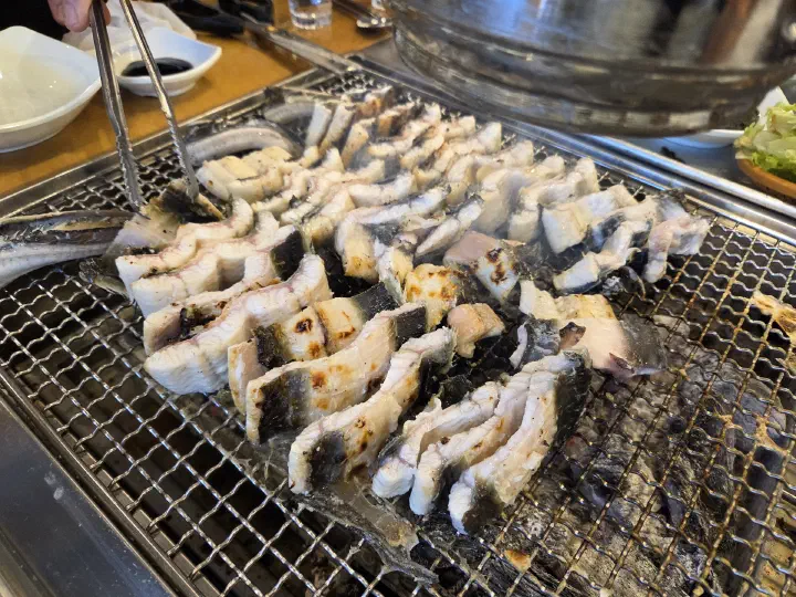 Grilling eel and flipping it with tongs until golden