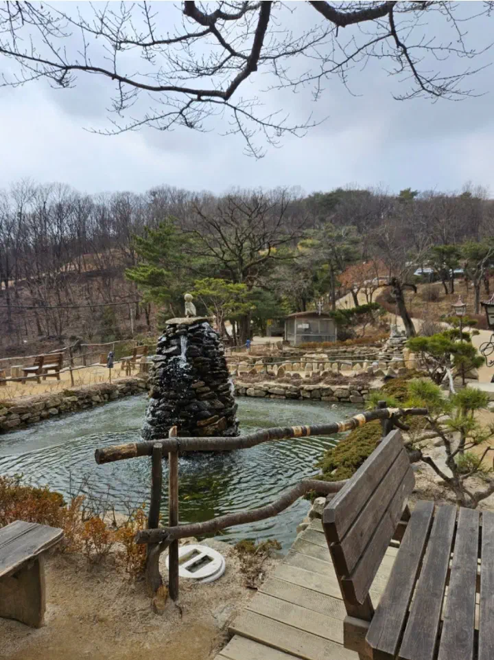 Wooden benches beside the stone tower fountain and pond in the Mokhyangwon garden