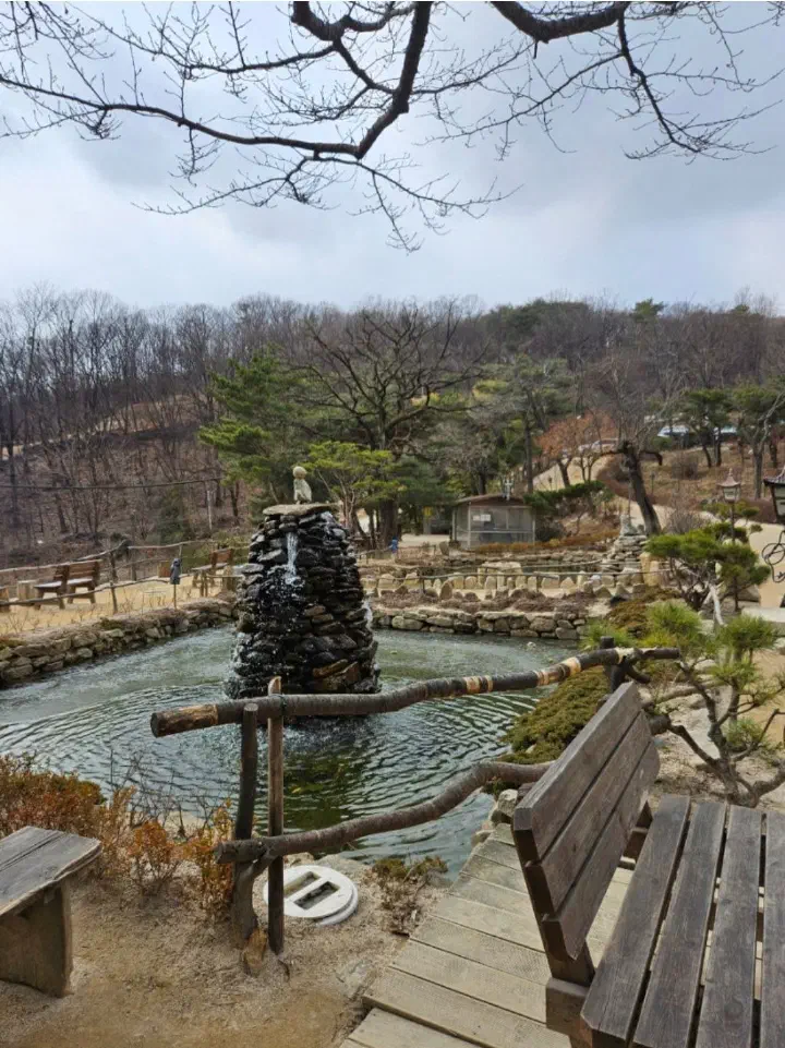 목향원 정원의 돌탑 분수와 연못, 산자락이 보이는 나무 벤치 쉼터