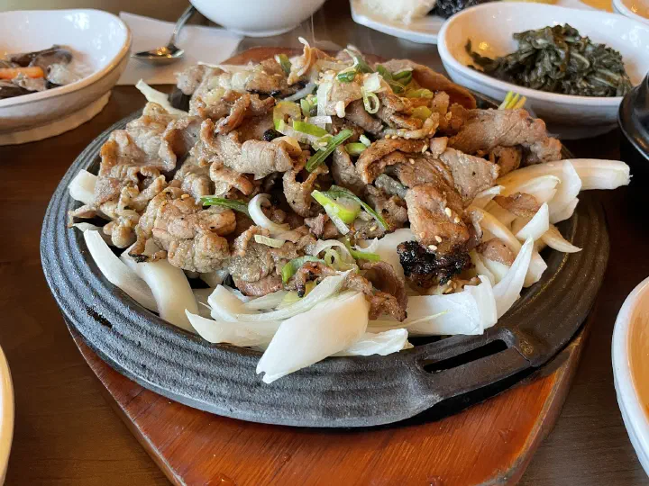 Mokhyangwon grilled pork plate surrounded by Korean side dishes of seasoned greens and mushrooms