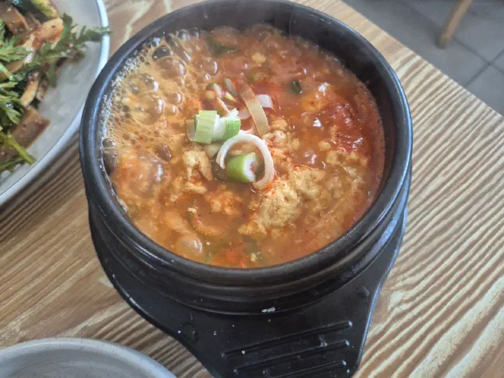 끓고 있는 백년옥 뚝배기 순두부 클로즈업, 붉은 국물 위에 대파와 순두부