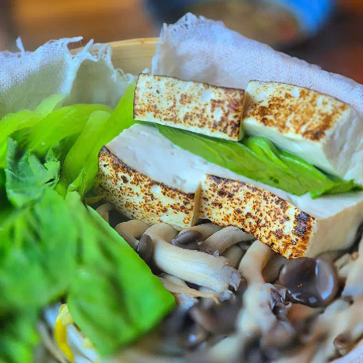 Close-up of grilled house-made tofu slices and shimeji mushrooms in the steamer