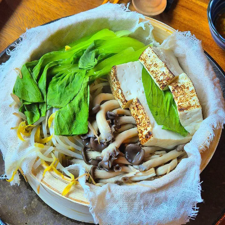 Steamed tofu with vegetables served in a bamboo steamer basket with mushrooms and bok choy