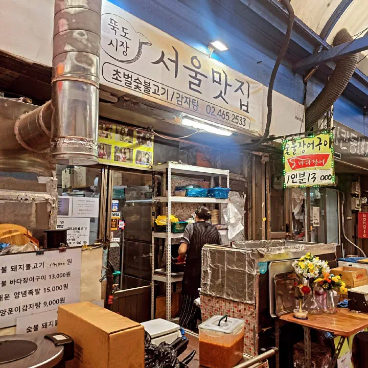 Handwritten price list and charcoal eel sign hanging in the Ttukdo Market alley