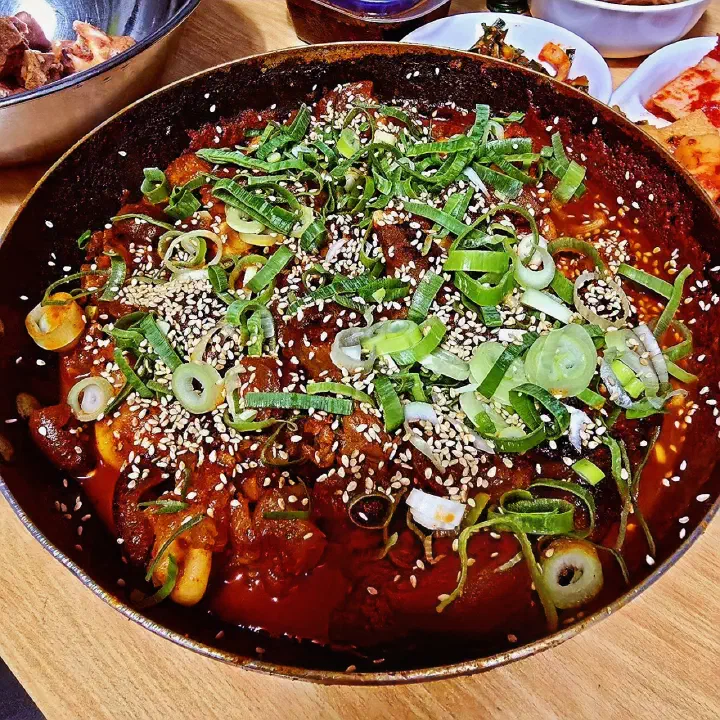 Spicy braised pig&rsquo;s trotters served in a wide pot under a heap of sliced scallions