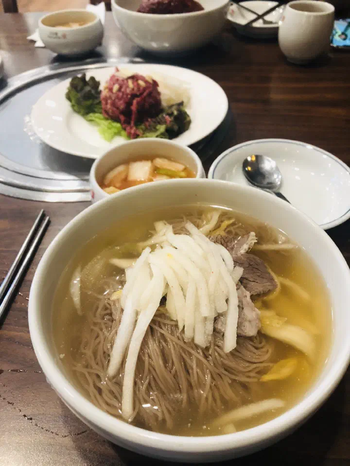 Table setting at Woo Lae Oak with a bowl of Pyongyang naengmyeon, geotjeori kimchi and a plate of Hanwoo beef tartare
