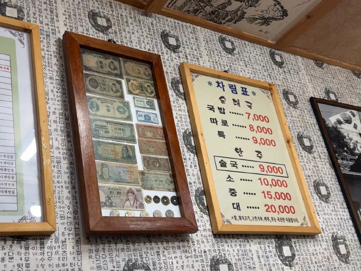 Interior wall of Samgeori Meonjimak Sundaeguk hung with framed vintage Korean currency and the menu board