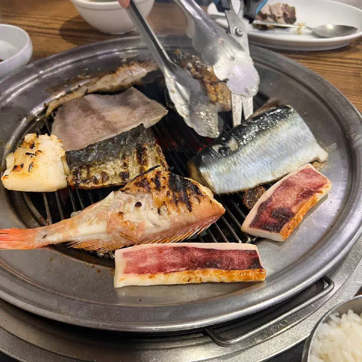 88생선구이 직원이 집게로 숯불 위 생선을 뒤집어 구워주는 모습