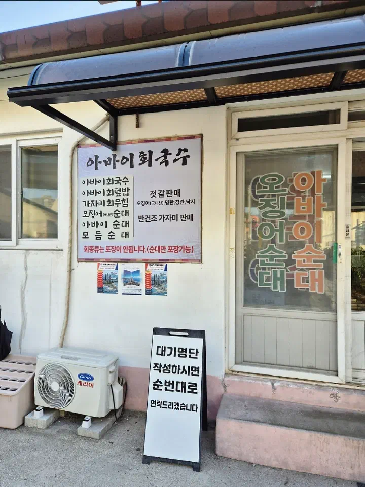 속초 아바이회국수 가게 외관의 메뉴 현수막과 대기명단 작성 안내 입간판