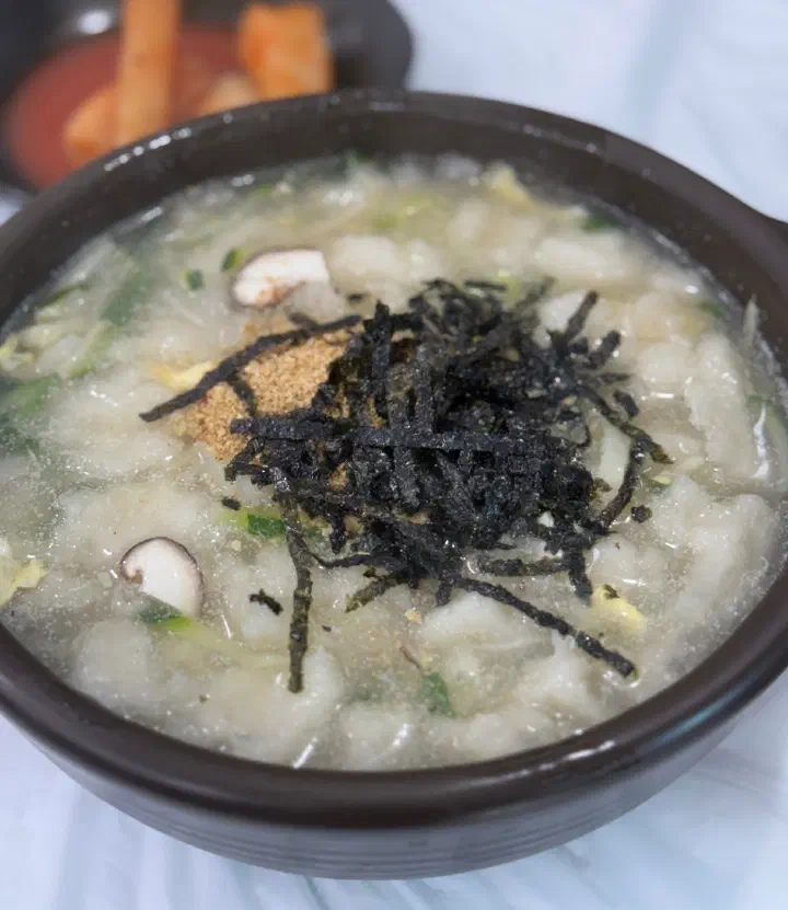 Close-up of gamja ongsimi broth with enoki and shiitake mushrooms and sliced zucchini