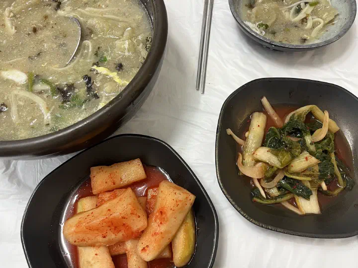 비닐을 깐 테이블 위에 차려진 감자옹심이 뚝배기와 앞접시, 밑반찬