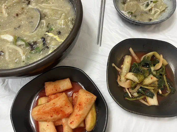 Gamja ongsimi pot, small serving bowls and side dishes on a plastic-sheeted table