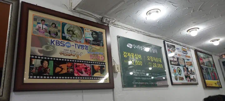 Framed KBS TV feature and menu board hanging on the wall inside Gamnamujip