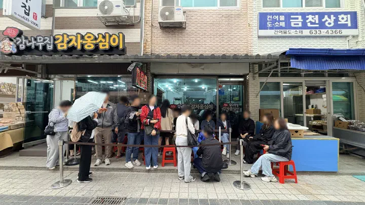 Customers waiting on red plastic chairs outside Gamnamujip Gamja Ongsimi in Sokcho Jungang Market