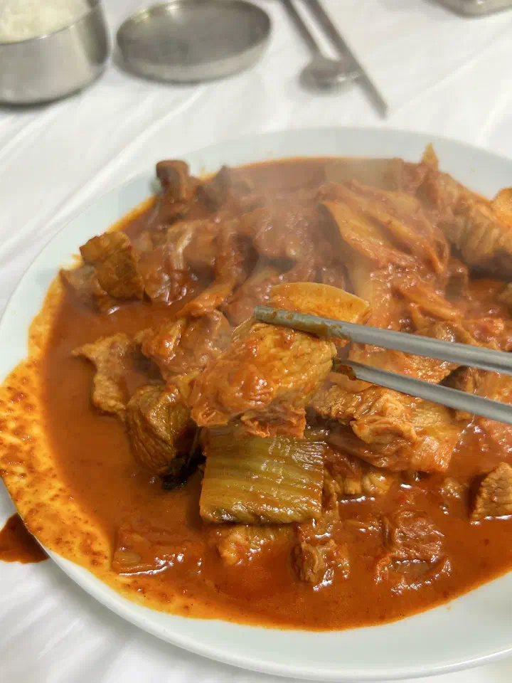 Chopsticks lifting pork from a steaming plate of duruchigi