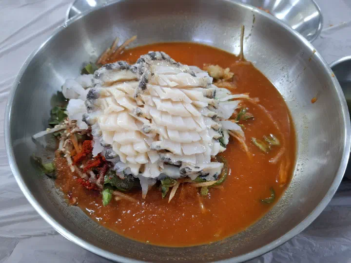 붉은 초장 육수 위에 채 썬 무와 오이, 청양고추가 보이는 산오징어물회 위에서 본 모습